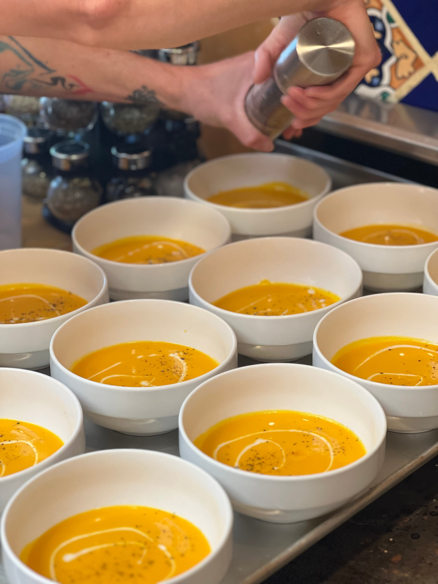 Chef Daniel finishing bowls of golden squash soup with cracked pepper